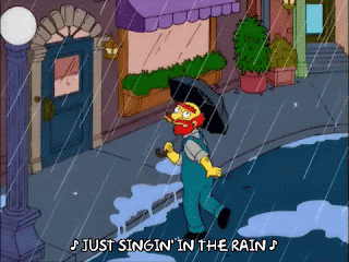 A gif of Groundskeeper Willie from The Simpsons is dancing in a street, swinging around a lamp post, as it rains.