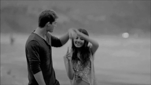 GIF of a young woman pulling a young man's arm around her shoulders
