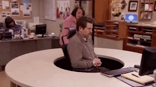 A gif from Parks and Recreation. Ron Swanson is sitting at his new desk. It is circular, with his chair in the centre of the circle, meaning he can be approached and seen from 360 degrees. A woman ha approached the desk and is trying to talk to him. He urns his chair around, in a continual cicurla motion, as she runs around the outside of the desk to get his attention. At no point does she see anything other than his back.