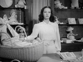 A black and white gif of a 1950s looking woman robotically rocking a baby's basket. She looks like she's on the edge.