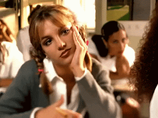Britney Spears, dressed as a school pupil sitting at her desk, in the Oops I Did It Again video. She looks bored shitless.