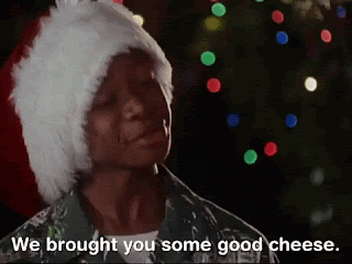 A kid in a Santa hat is standing in front of someone off camera. The caption says, 'We bought you some good cheese.'