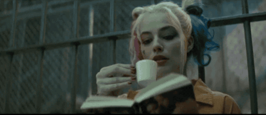 Harley Quinn in a prison cell, reading and sipping tea.