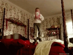 Kevin from Home Alone is jumping on his parent's double bed, wearing his clothes and shoes, and holding a box of cream that's being spilt all over the bed.