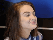 A smiling white woman, with brunette hair and closed eyes, has approximately ten McDonalds chicken nuggets thrown at her face.