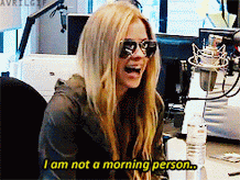 A blonde white women (Avril Lavigne) is sitting infront of a computer, wearing a hoody and sunglasses. The caption reads, 'I'm not a morning person.'