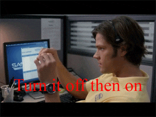 A man sits at a computer at a help desk looking board as he speaks into his headphone mic. The caption reads, 'Turn it off and on again.''