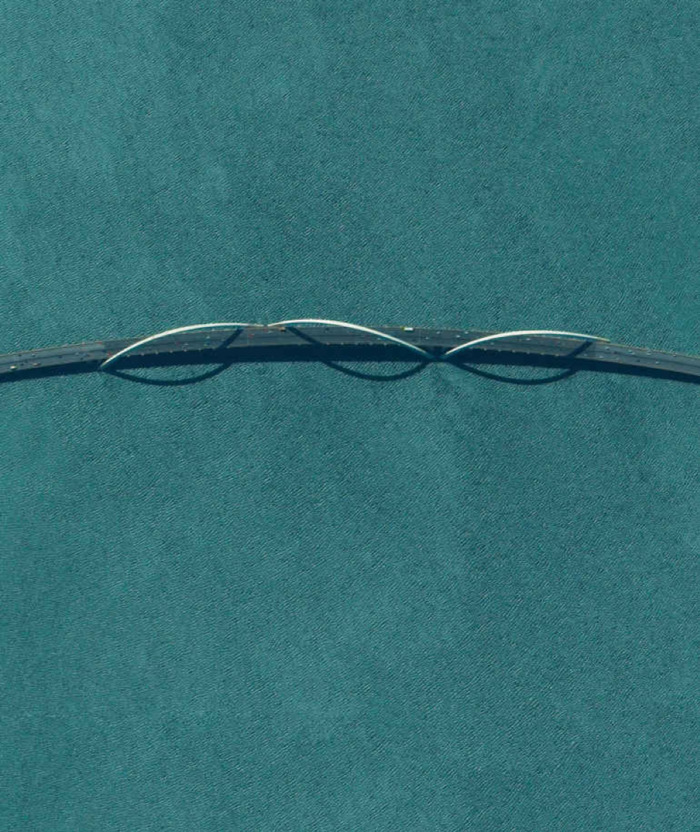 a strip dark gray bridge over a teal ocean. it has thin silver arches.