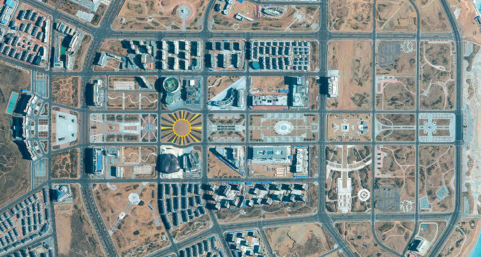 a city grid, mostly sandy or grey concrete. in the center there’s a city block with a yellow circle which has yellow, tan, and grey lines going outwards, which looks like a child’s drawing of a sun.